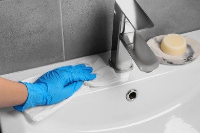 Photo of Woman in glove cleaning sink with paper towel, closeup