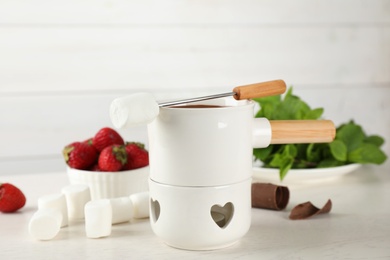Photo of Fondue pot with chocolate and marshmallow on white wooden table
