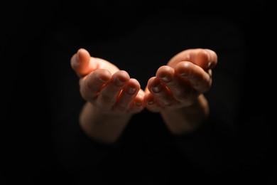 Photo of Religion. Woman with open palms praying on black background, closeup