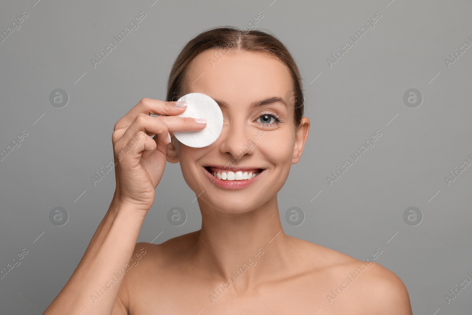 Photo of Smiling woman removing makeup with cotton pad on grey background