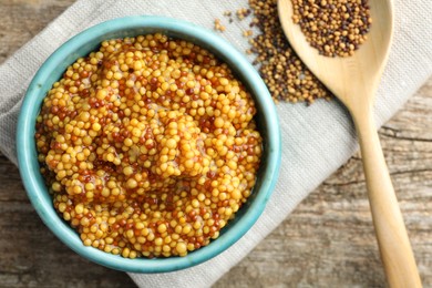 Photo of Fresh whole grain mustard in bowl and dry seeds on wooden table, flat lay