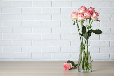 Photo of Vase with beautiful pink roses on wooden table. Space for text