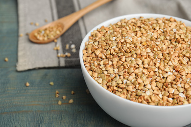 Photo of Uncooked green buckwheat grains in bowl on light blue wooden table, closeup