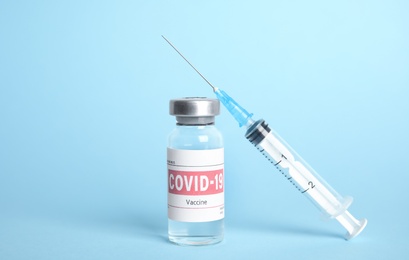 Vial with coronavirus vaccine and syringe on light blue background