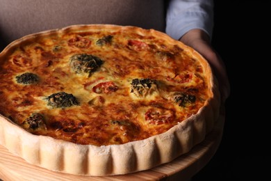 Photo of Woman holding delicious homemade vegetable quiche on black background, closeup