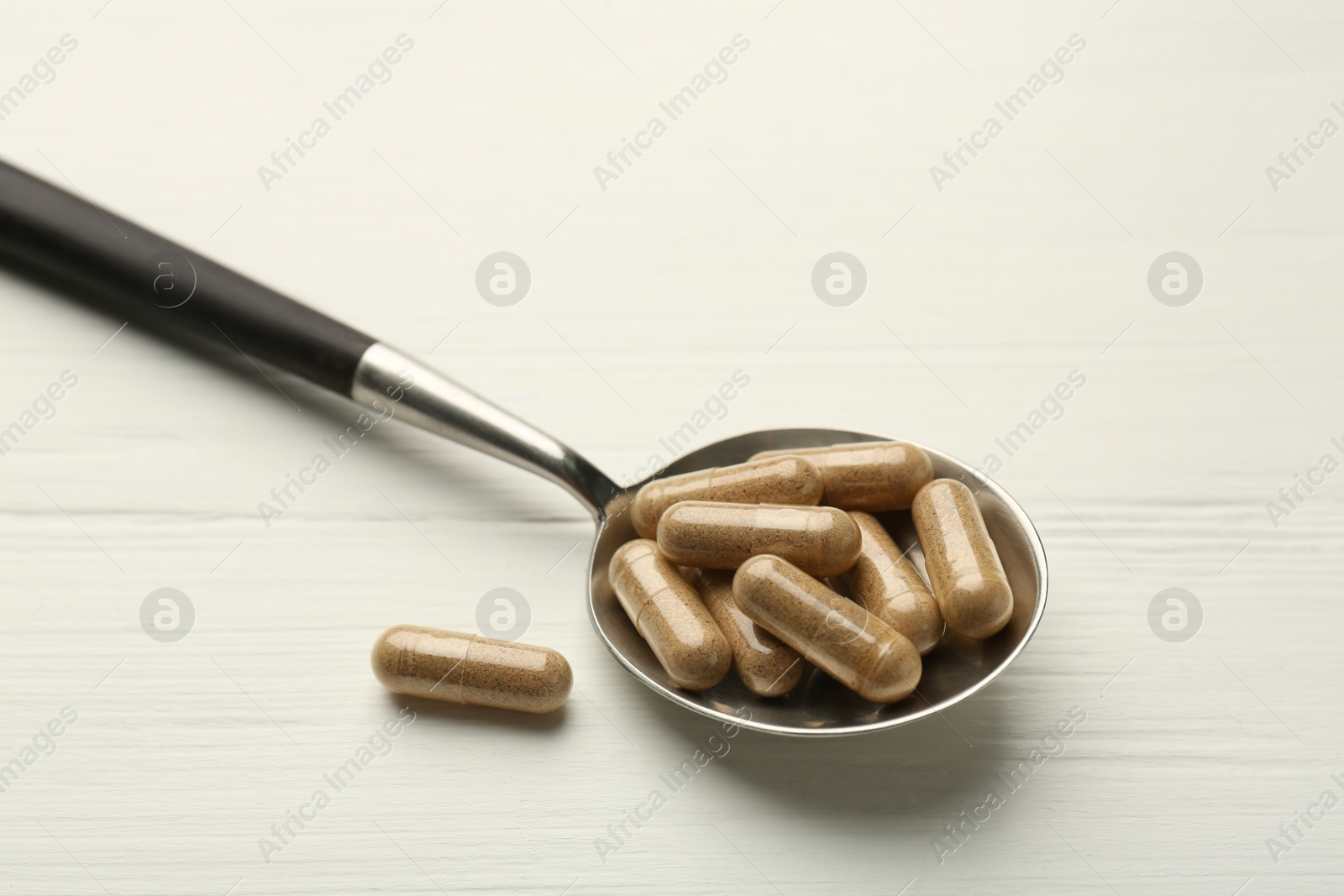 Photo of Vitamin capsules in spoon on white wooden table, closeup