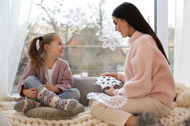 Photo of Mother and daughter decorating window with paper snowflakes at home