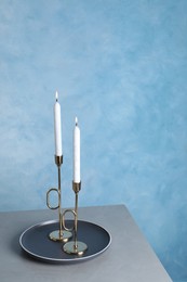 Photo of Holders with burning candles on grey table near light blue wall