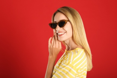 Photo of Beautiful woman in stylish sunglasses on red background. Space for text