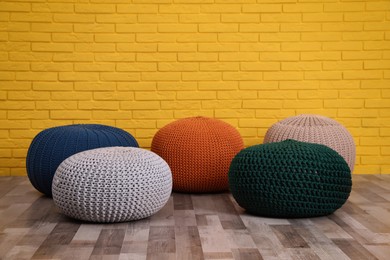 Photo of Many different stylish poufs on floor near yellow brick wall in room