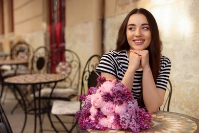 Photo of Beautiful woman with bouquet of spring flowers in outdoor cafe, space for text