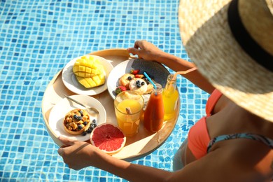 Photo of Young woman with delicious breakfast on floating tray in swimming pool, closeup