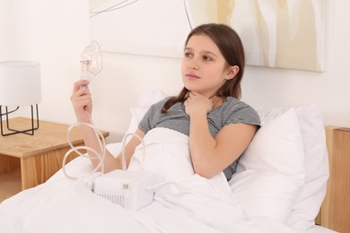 Photo of Cute girl holding nebulizer for inhalation on bed at home