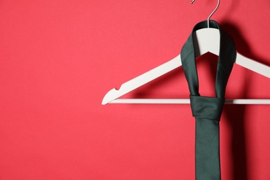 Photo of Hanger with black tie on red background. Space for text