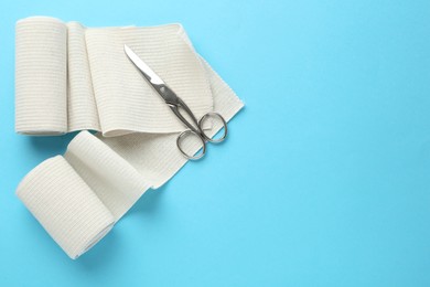 Photo of Medical bandage rolls and scissors on light blue background, flat lay. Space for text