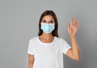 Photo of Woman in protective mask showing hello gesture on grey background. Keeping social distance during coronavirus pandemic