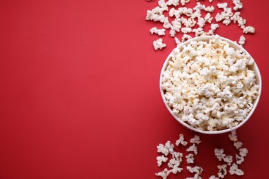 Photo of Paper bucket and delicious popcorn on red background, flat lay. Space for text