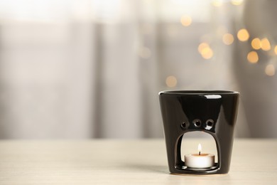 Photo of Aroma lamp with burning candle on table against blurred lights, space for text