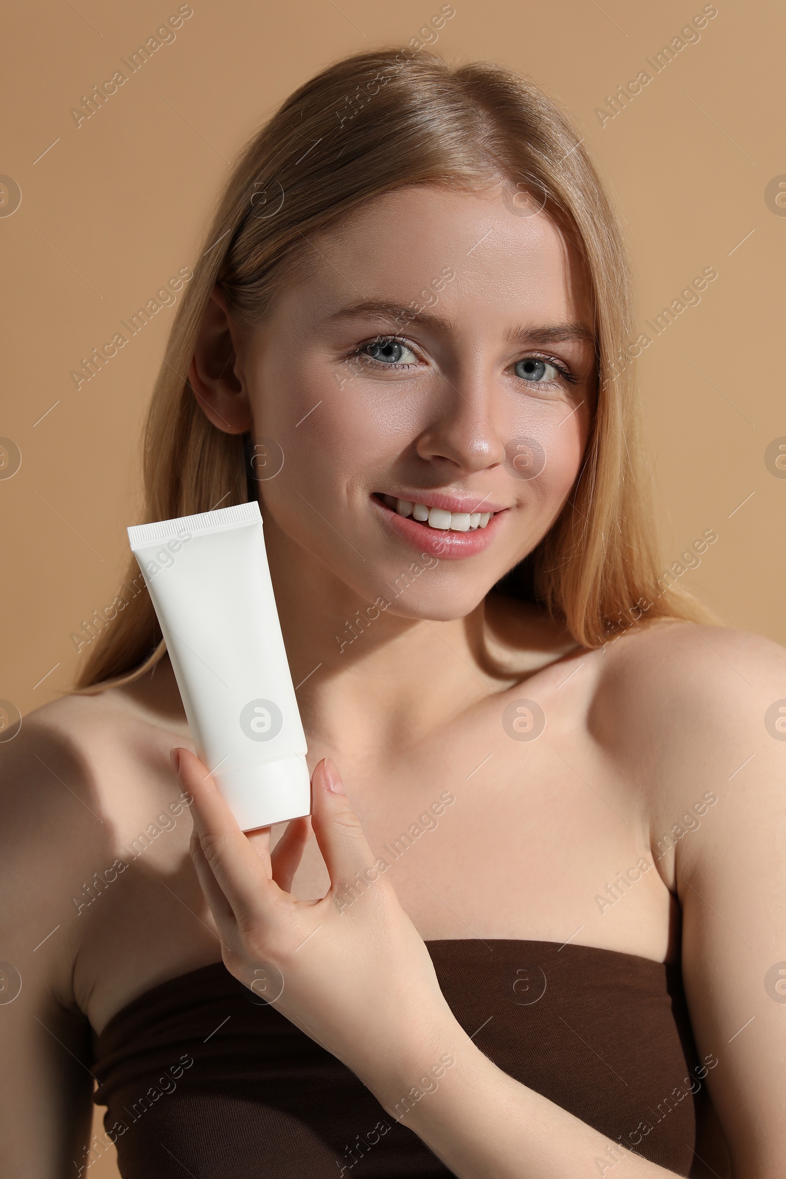 Photo of Beautiful young woman holding sun protection cream on beige background