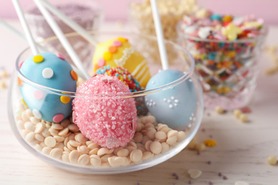 Photo of Egg shaped cake pops for Easter celebration on white wooden table, closeup