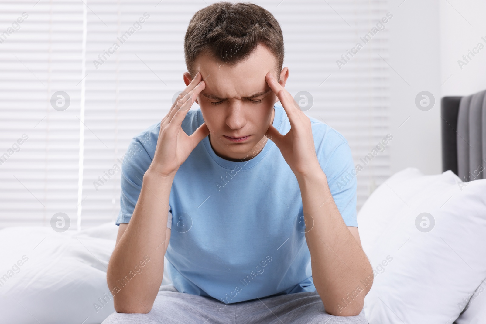 Photo of Sad man suffering from headache on bed indoors