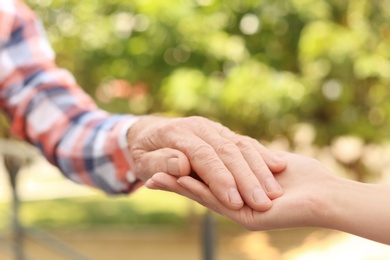 Photo of Helping hands on blurred background, closeup. Elderly care concept