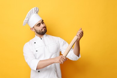Photo of Professional chef with rolling pin on yellow background