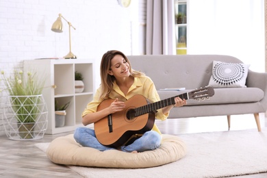 Photo of Young woman playing acoustic guitar in living room