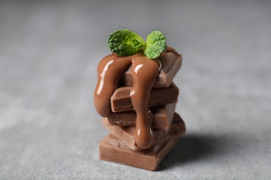 Photo of Pieces of milk chocolate with tasty paste and mint on gray table, closeup