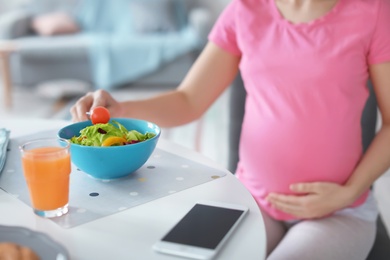 Photo of Young pregnant woman eating vegetable salad at table in kitchen