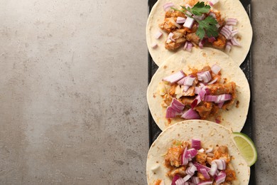 Photo of Delicious tacos with vegetables, meat and lime on grey textured table, top view. Space for text