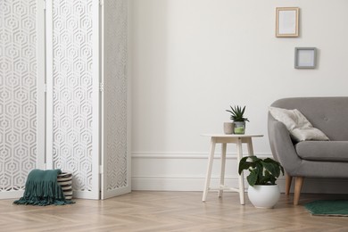 Photo of Stylish room with folding screen and sofa near white wall. Interior design