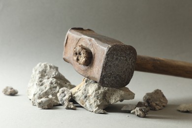 Photo of One sledgehammer and pieces of broken stones on grey background, closeup