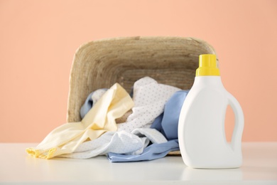 Photo of Detergent and children's clothes on white table near pink wall