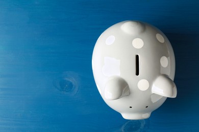 Ceramic piggy bank on blue wooden table, top view. Space for text