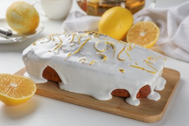 Photo of Tasty lemon cake with glaze and citrus fruits on white table