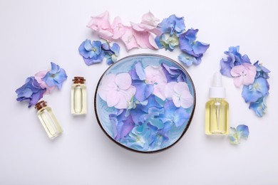 Photo of Spa composition. Aromatic water in bowl, flowers and bottles of essential oil on white background, flat lay