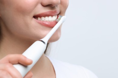 Photo of Woman brushing her teeth with electric toothbrush on white background, closeup. Space for text