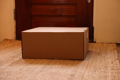 Photo of Delivery service. Cardboard on rug near wooden door indoors