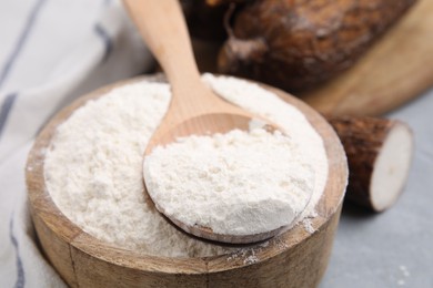 Photo of Wooden bowl and spoon with cassava flour on grey table, closeup