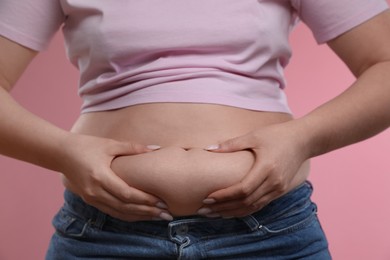 Photo of Woman touching belly fat on pink background, closeup. Overweight problem