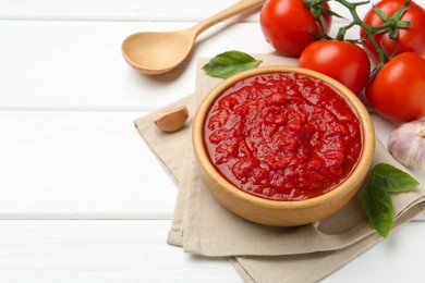 Photo of Homemade tomato sauce in bowl, spoon and fresh ingredients on white wooden table. Space for text