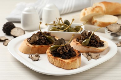 Photo of Delicious bruschettas with truffle sauce and caperberries on white wooden table, closeup