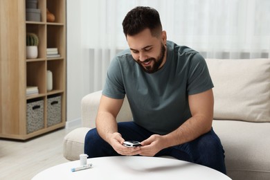 Photo of Diabetes test. Smiling man with glucometer at home