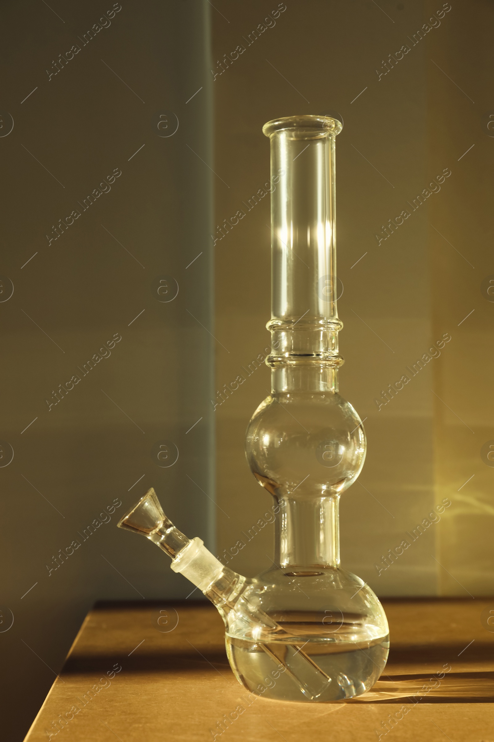 Photo of Glass bong on wooden table indoors. Smoking device