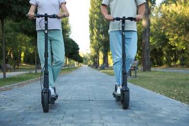 Couple riding modern electric kick scooters in park, closeup