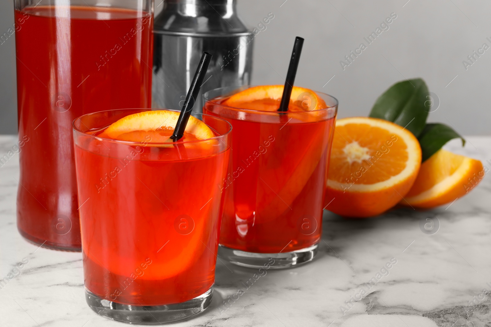 Photo of Aperol spritz cocktail, orange slices and straws in glasses on white marble table, closeup