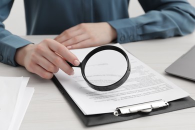 Woman looking at document through magnifier at white wooden table, closeup. Searching concept