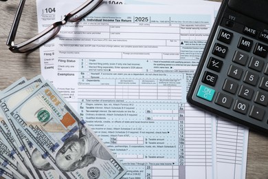 Payroll. Tax return forms, dollar banknotes, glasses and calculator on wooden table, flat lay