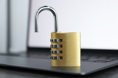 Photo of Cyber security. Metal combination padlock and laptop on table, closeup